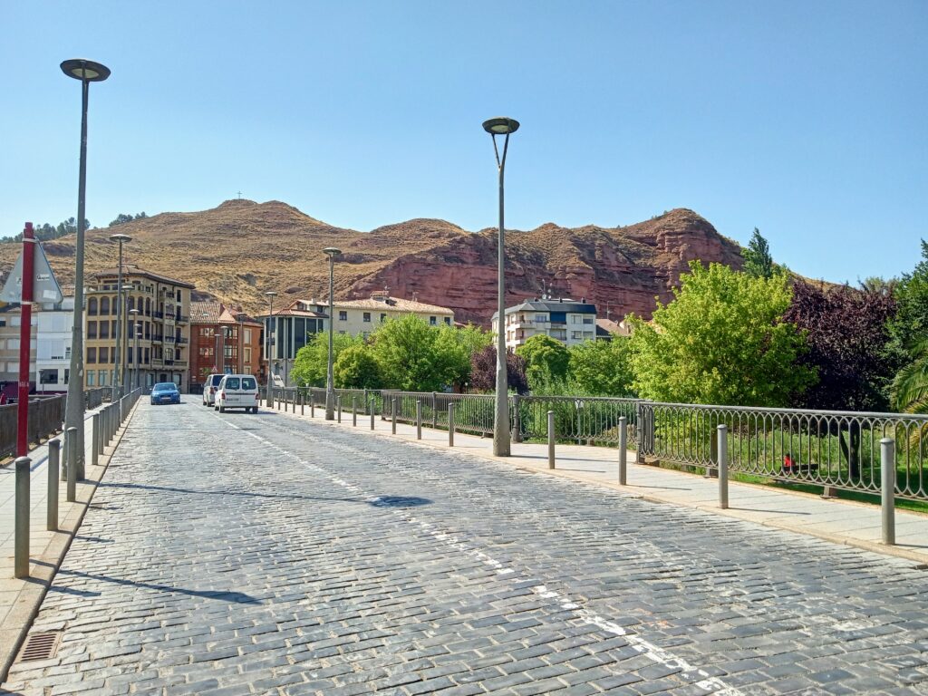 A bridge leads into town with terracotta mountains.