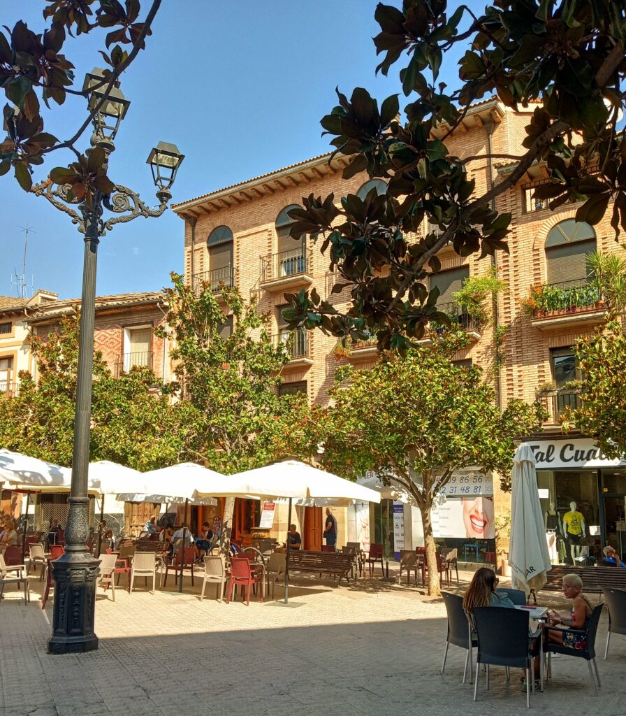 An outdoor plaza with old-fashioned lamp posts, buildings and tables with umbrellas.